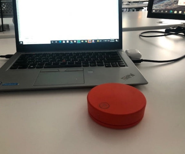 Laptop on a desk beside a red circular device.